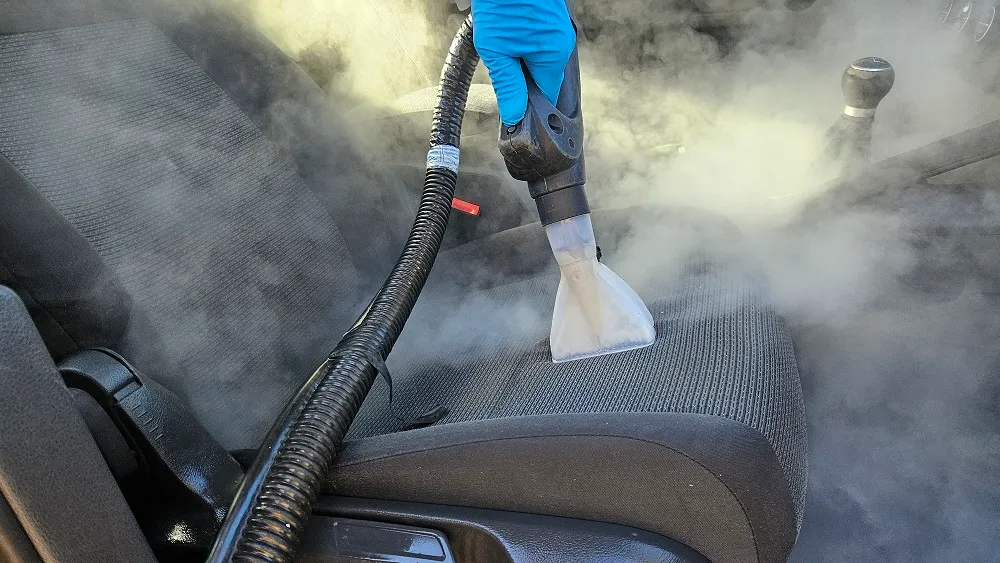 Accesoriu transparent de curățare aplicat pe șezutul textil al scaunului auto, printre vapori.
