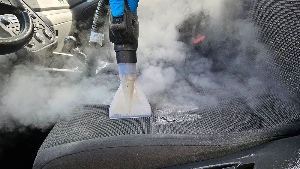 Cap transparent al unui echipament de curățare aplicat pe șezutul scaunului auto, cu vapori în jur.